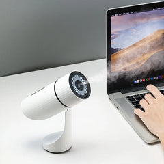 White desk fan next to a laptop on a white surface with a gray background