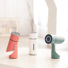 Three portable fans in pink, white, and green on a light surface with a blurred background.