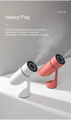 Two humidifier devices, one white and one pink, emitting heavy fog on a gray background.
