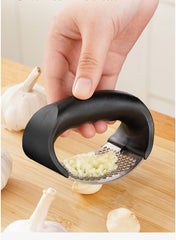Hand using a garlic press on a wooden surface with garlic cloves.