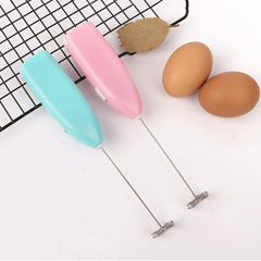 Two colorful egg beaters on a white surface with two eggs.