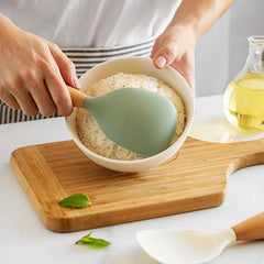 Person using a green silicone spatula to mix ingredients in a bowl on a wooden cutting board.