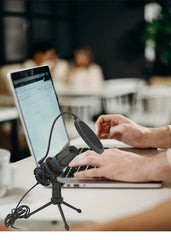 Person using a laptop with a microphone on a tripod in an office setting