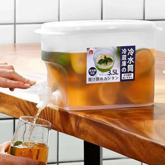 Person pouring tea from a large container into a glass on a wooden table.