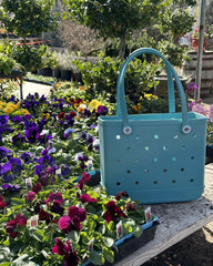 Blue handbag with polka dot pattern on a wooden surface surrounded by colorful flowers.