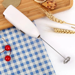 White whisk on a blue and white checkered tablecloth with wheat stalks and red cherries.