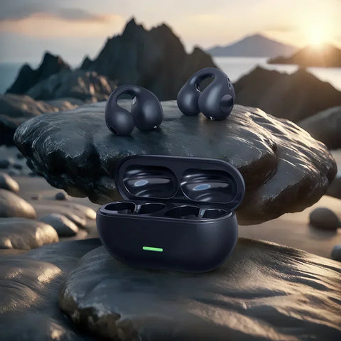 Black wireless earbuds with charging case on a rocky beach at sunset