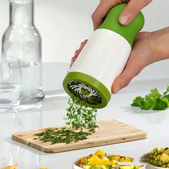 Hand using a green and white herb grinder to sprinkle chopped herbs onto a dish.