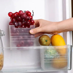 Hand placing a container of grapes into a refrigerator with other fruits.