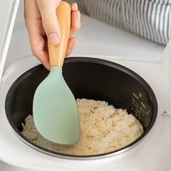 Green silicone spoon with wooden handle being used to scoop rice from a rice cooker.