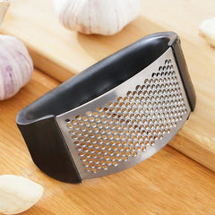 Metal garlic press on a wooden surface with garlic cloves and shells.