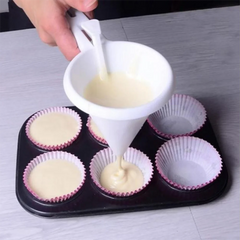 Person using a funnel to pour batter into cupcake liners on a baking tray.