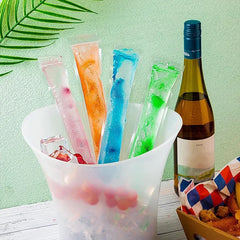 Colorful ice pops in a bucket with a bottle of wine and snacks on a light green background