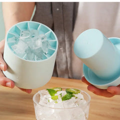 Person using a ice cube tray to add ice to a drink on a wooden surface