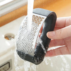 Hand holding a black and silver kitchen grater under running water.