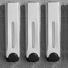 Three metallic soap dispensers with black bases on a gray stone background