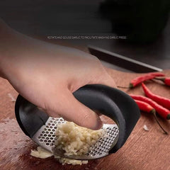 Hand using a garlic press on a wooden surface with red chili peppers.