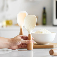 Person holding a wooden-handled rice paddle with a bowl of rice in the background