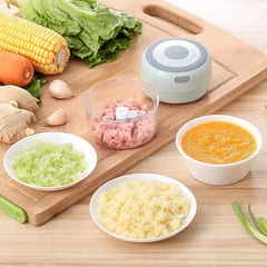 Small food processor on a wooden cutting board with various ingredients and processed foods.