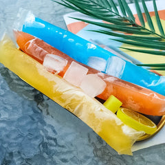 Two popsicles, one orange and one yellow, with lemon slices on a marble surface.