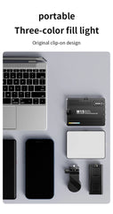Three-color fill light with clip-on design on a gray surface with laptop, phone, and other items.