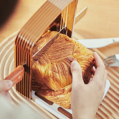 Person cutting a croissant with a knife on a wooden board.