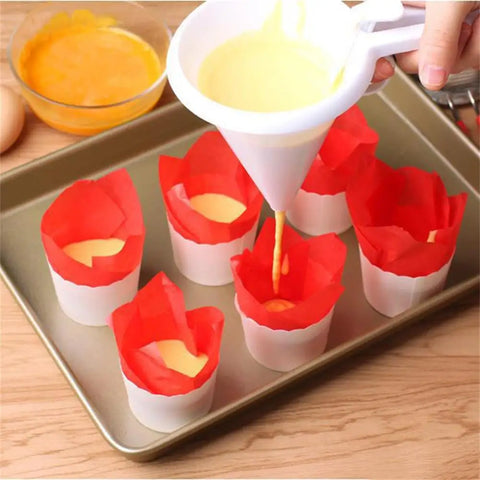 Funnel being used to pour liquid into red paper cups on a baking sheet.