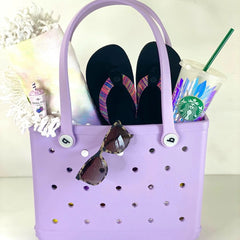 Purple tote bag with flip-flops, sunglasses, and a Starbucks cup on a white surface.