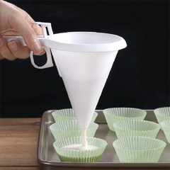 White funnel being used to pour batter into green cupcake liners on a baking sheet.