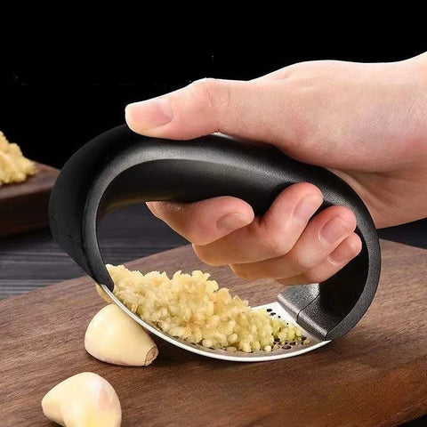 Hand using a garlic press on a wooden surface with garlic cloves around