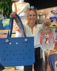 Woman holding a blue perforated bag and a pair of sandals in a store setting